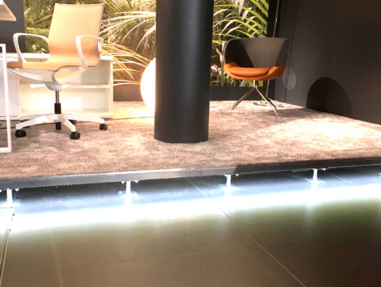 Beleuchtetes Doppelbodensystem mit Teppichbelag und sichtbarer LED-Unterbodenbeleuchtung in einem modernen Showroom von MM Doppelboden.