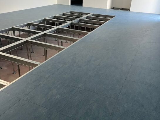 Weitläufiger, fertig verlegter Doppelboden in Blau-Grau mit sichtbarer Unterkonstruktion an den Seitenrändern von MM Doppelboden.